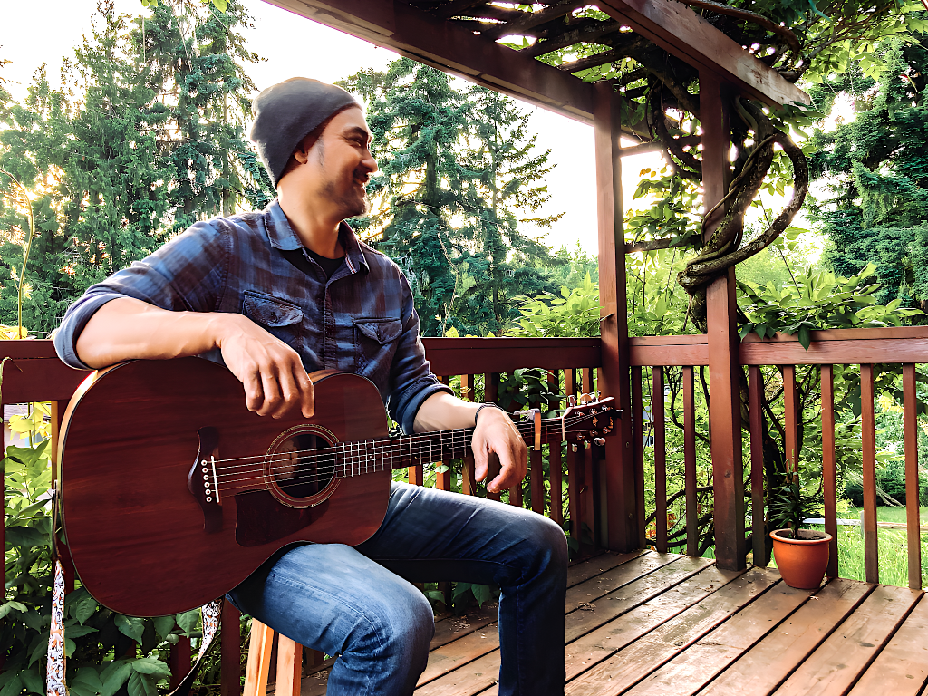 Michellion playing acoustic guitar amidst the greenery